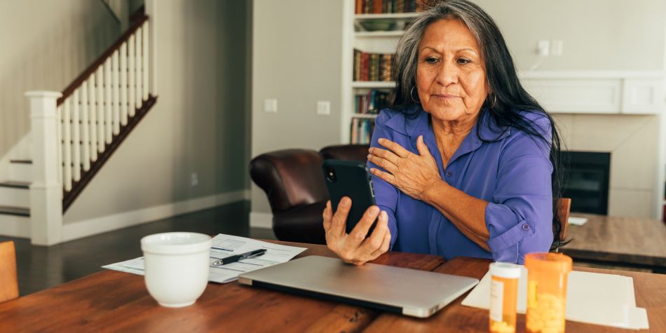 A senior aged woman sits at her kitchen table while talking on the phone with her doctor, and updating medicine prescriptions.